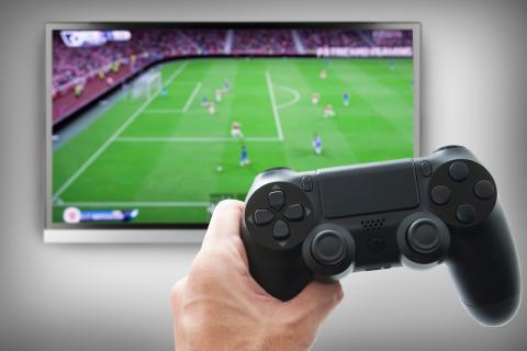 Der Benutzer hat sich mit einem Controller an einer Videospielkonsole angemeldet, um ein Fußballspiel zu spielen, das auf dem Bildschirm angezeigt wird.