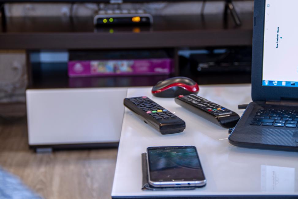 A TV screen with a set-top box in the background which are steered by two TV remotes and a smartphone lying on a table; a login to a content service is performed by the user.