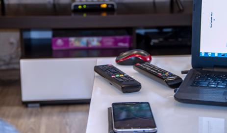 A TV screen with a set-top box in the background which are steered by two TV remotes and a smartphone lying on a table; a login to a content service is performed by the user.