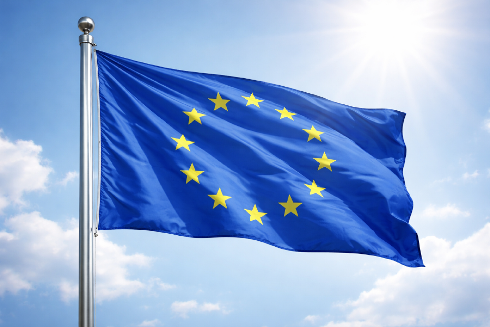 The Blue Flag of the European Union with its twelve golden stars moving in the wind on a flagpole, with the sun shining in the background.