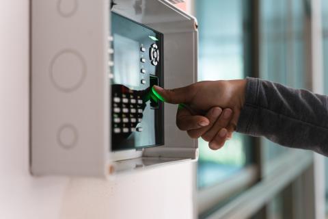 Person loggt sich an einem an der Wand hängenden biometrischen Zugangssystem mittels Fingerabdruck ein.