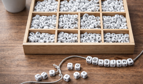 In einer Holzkiste liegen Perlen mit jeweils unterschiedlichen Buchstaben, Zahlen und Sonderzeichen, davor eine Schnur, auf der bereits einige Perlen aufgereiht wurden und ein Passwort ergeben.